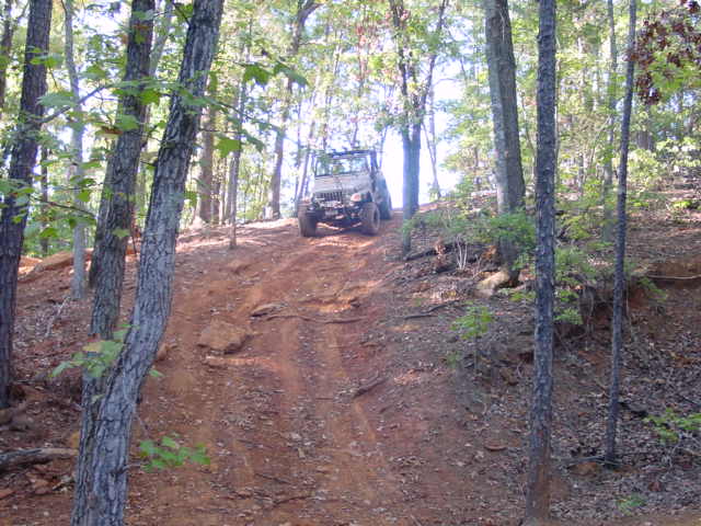 Jeep Wrangler climbing a steep, wooded dirt trail. It's a 2004 Jeep TJ