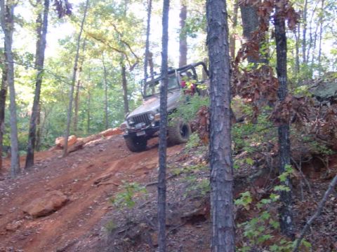 2004 Jeep Wrangler - A silver Jeep Wrangler TJ navigates an off-road trail, ascending a steep, red dirt incline surrounded by trees.
