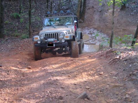 2004 Jeep Wrangler - A Jeep TJ navigates a challenging off-road trail with muddy terrain and wooded surroundings.
