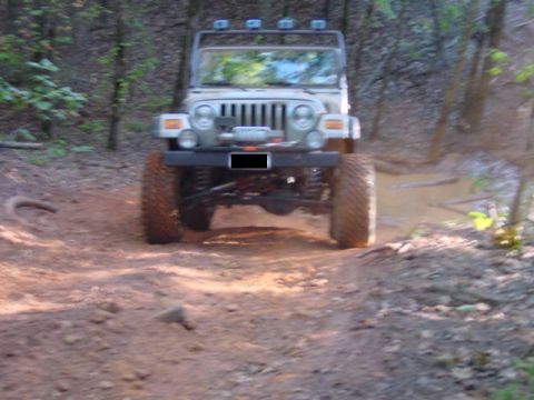 2004 Jeep Wrangler - A modified 2004 Jeep Wrangler navigates a muddy trail through a wooded area.