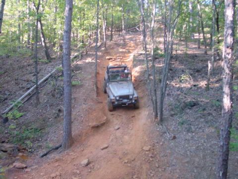 2004 Jeep Wrangler - A silver Jeep Wrangler navigates an off-road trail, climbing a steep, rutted dirt path surrounded by trees.