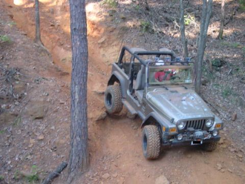 2004 Jeep Wrangler - A Jeep TJ navigates a steep, rutted dirt path surrounded by trees.