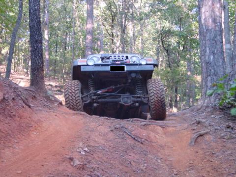 2004 Jeep Wrangler - A Jeep TJ navigates a dirt trail in a wooded area, showing its rear suspension and large tires.
