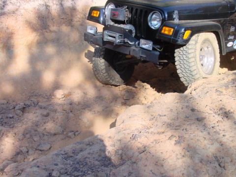 2004 Jeep Wrangler - A black Jeep TJ navigates a challenging off-road obstacle, with one wheel dropping into a deep rut.
