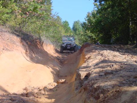 2004 Jeep Wrangler - A Jeep Wrangler TJ navigates a steep, sandy incline on an off-road trail surrounded by trees.