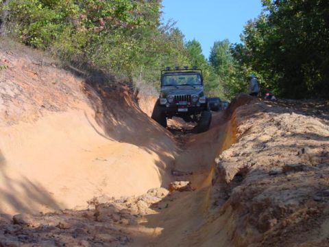 2004 Jeep Wrangler - A Jeep TJ navigates a steep, sandy off-road trail, kicking up dirt as it goes.