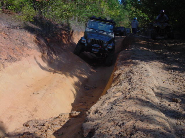 Black Jeep TJ driving down a sandy ditch, front-left wheel angled up