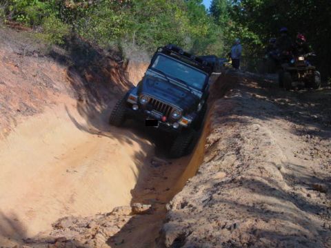 2004 Jeep Wrangler - A black Jeep Wrangler TJ navigates a challenging dirt trail, while an ATV and onlookers observe from higher ground.