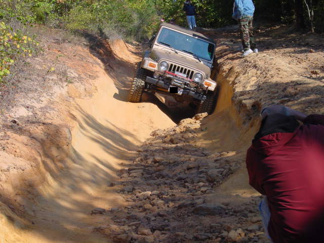 2004 Jeep TJ navigating a steep dirt rut on an off-road trail