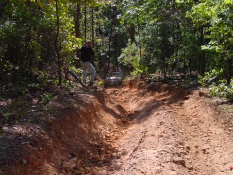 2004 Jeep Wrangler - A person stands on the edge of a steep dirt trail while an off-road vehicle navigates the path.