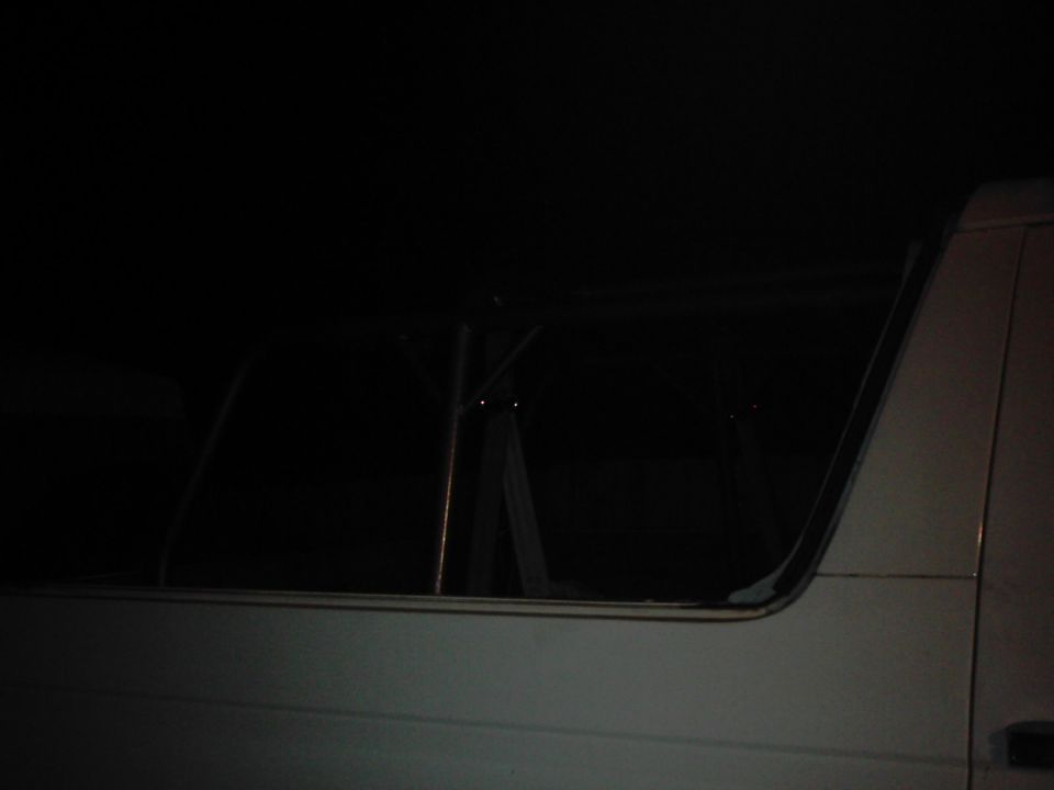 Interior view of a vehicle, showing window frames and roll cage structure in darkness