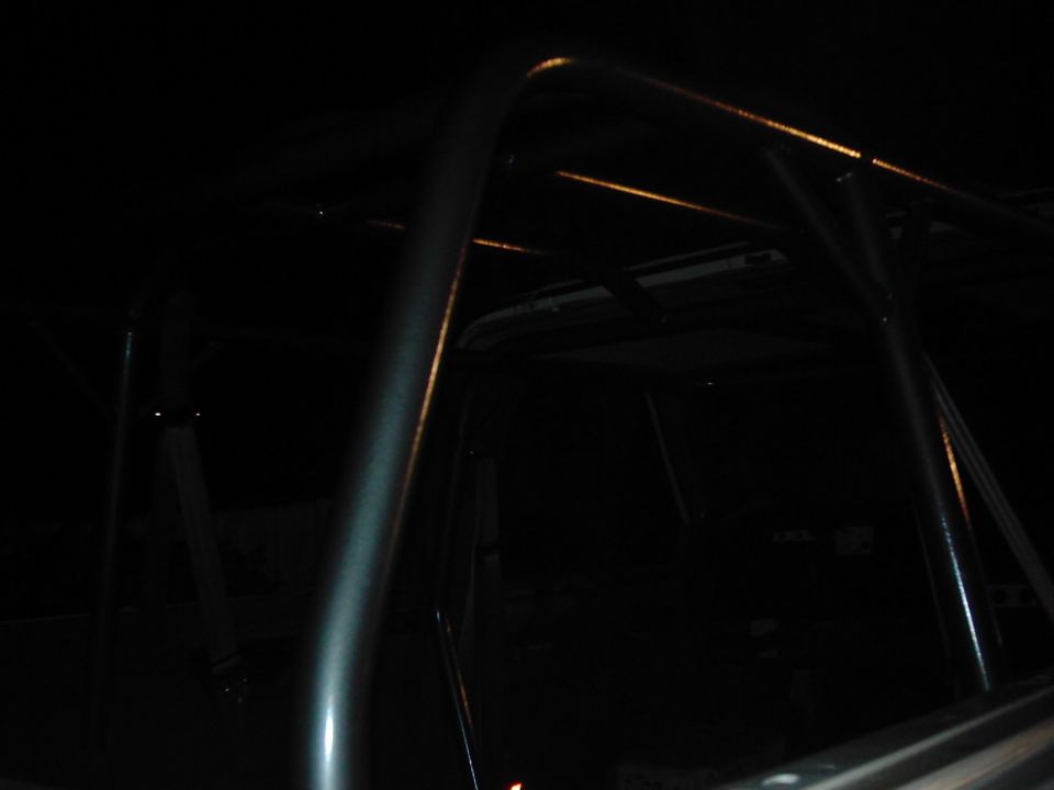 Interior view of a vehicle with a metal roll cage installed. Some lights reflect off the bars