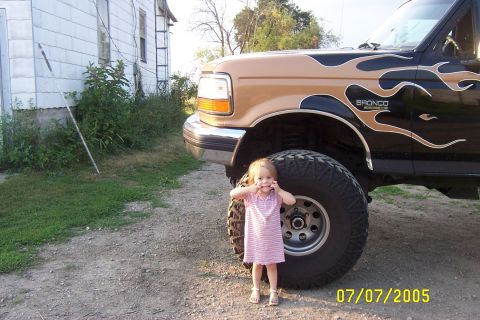 1995 Ford Bronco with flame decals and a young child standing next to the front tire