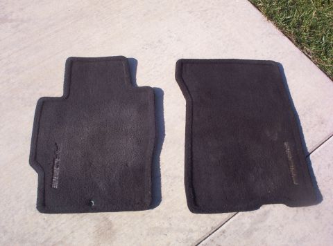 1994 Ford Probe - Two black carpeted floor mats are shown outdoors on a concrete surface next to grass.
