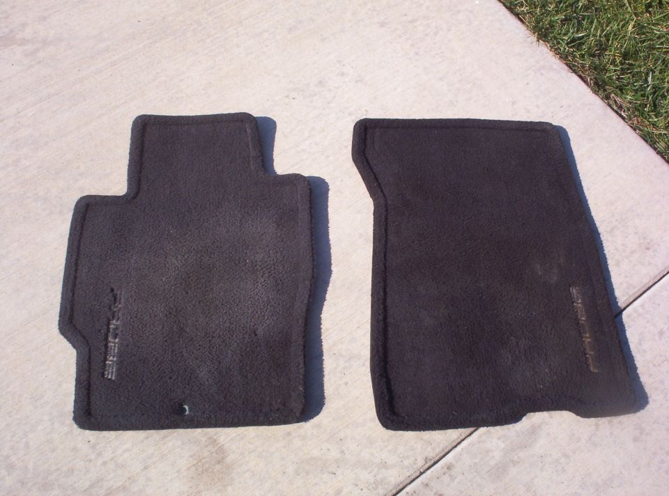 two black car floor mats, one with a T-shaped top, both have embossed text