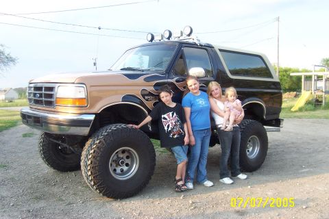 1995 Ford Bronco with flame decals and large tires, viewed from the front-three-quarter angle