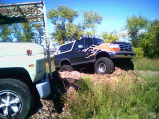 Ford Bronco with flame decals driving up a dirt mound next to another vehicle