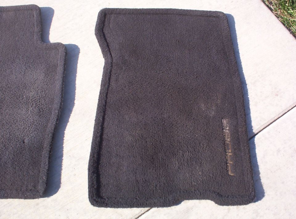 two dark gray car floor mats, one with faint embossed text on the right side