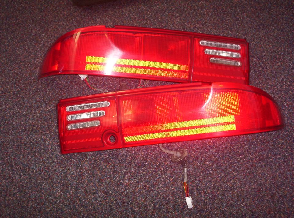 Pair of red car tail lights with yellow reflectors and wiring harnesses
