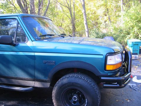 1996 Ford Bronco - A teal Ford Bronco is parked outdoors with trees in the background. The front fender and bumper area are visible.
