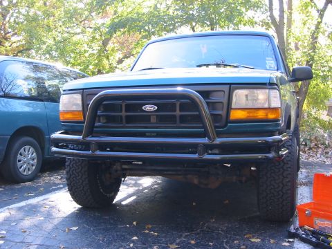 1996 Ford Bronco - Front view of a green Ford Bronco with a bull bar and aftermarket bumper, parked next to a blue van.