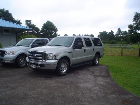 2005 Ford Excursion - Two silver Ford vehicles, an Excursion and an F-150, are parked on a driveway in front of a building.