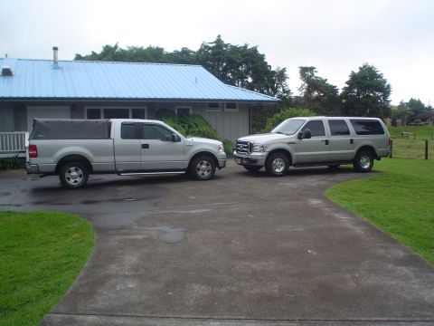 2005 Ford Excursion - A silver 2005 Ford Excursion is parked on a driveway next to a silver Ford F-150 pickup truck.