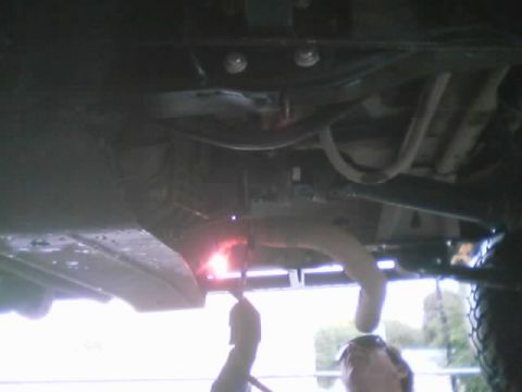 1990 Ford Bronco - Underside view of a vehicle being welded, with a bright arc and sparks near the frame rails, skid plate and exhaust pipe.