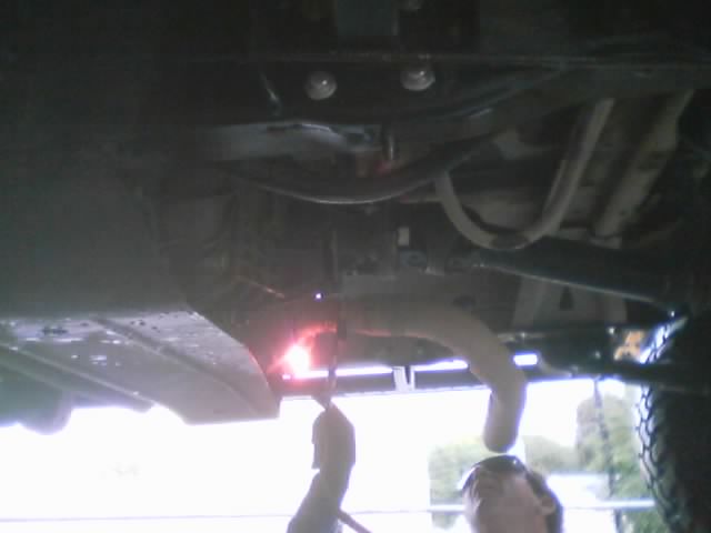 Underside of a vehicle during welding with bright sparks near the frame and exhaust