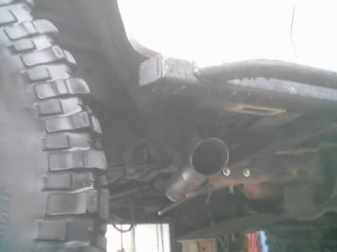 1990 Ford Bronco - Underbody view of a lifted truck showing the angled exhaust pipe tip, frame rail and a deep-lug mud-terrain tire.