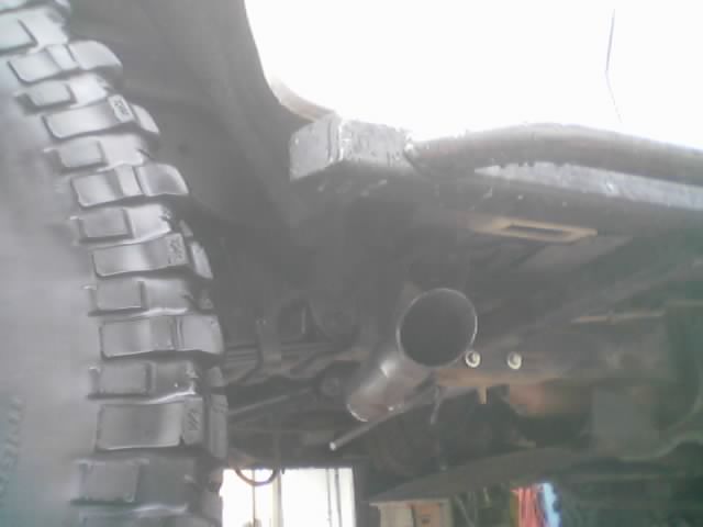 Underside of a lifted truck showing exhaust pipe tip, frame and mud-terrain tire