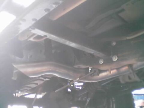 1990 Ford Bronco - Underbody view of a vehicle showing the frame rails, a crossmember with bushings, exhaust pipe and driveline components.