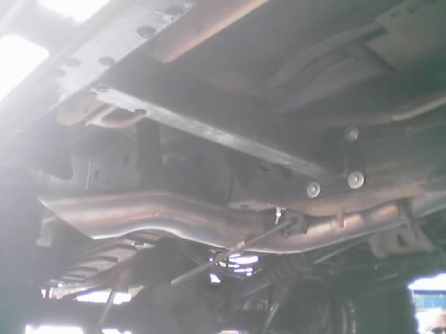 Underside of a vehicle showing frame rails, crossmember, exhaust pipe and driveline