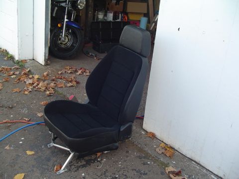 1994 Ford Bronco - A black car seat is positioned outside a garage, with fallen leaves scattered around it.