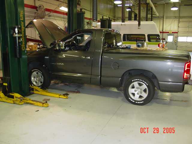 Gray Dodge Ram 1500 pickup with hood up in a repair shop, passenger side view.