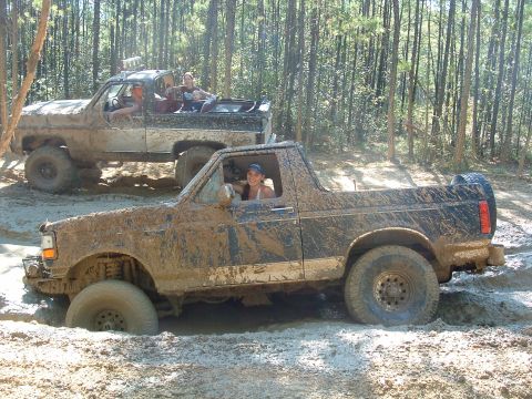 1993 Ford Bronco - Two off-road vehicles navigate a muddy trail, with the lead Bronco deeply stuck in the mire.