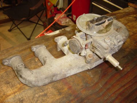 1991 Ford Bronco - A carburetor and intake manifold assembly rests on a wooden workbench, with "SUPERMOTORS.NET" visible at the bottom right.