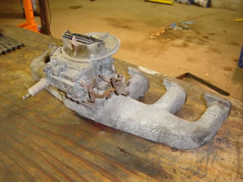 1991 Ford Bronco - Carburetor and exhaust manifold assembly, likely from a Ford vehicle, resting on a wooden surface.