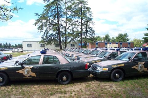 1991 Ford LTD Crown Victoria - Multiple state trooper vehicles are parked in a lot, lined up side-by-side under a partly cloudy sky.