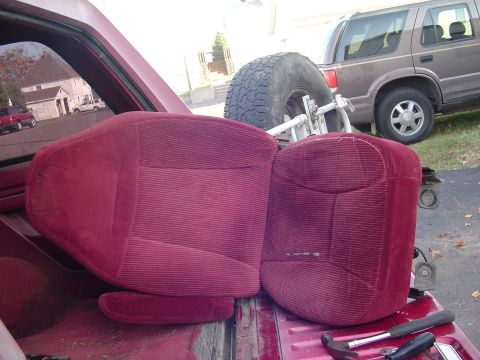 1994 Ford Bronco - Car seats and a spare tire are visible in the bed of a pickup, with an SUV parked nearby.