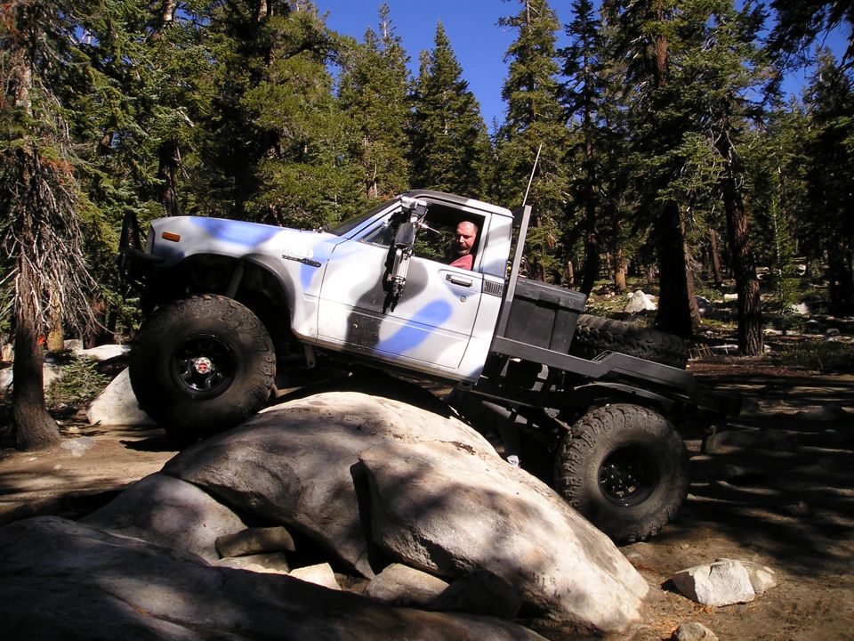 Modified pickup truck with large tires climbing over rocks in a forest
