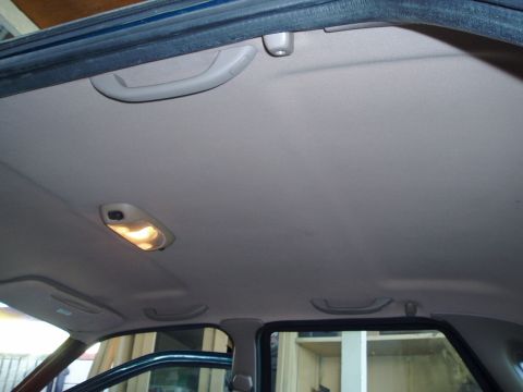 1995 Ford Taurus - Interior view of a car's headliner, grab handles and an illuminated dome light.