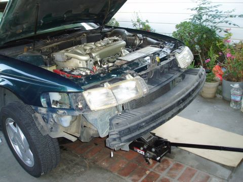 1995 Ford Taurus - The front end of a car is disassembled, revealing the engine and exposed components. A jack supports the vehicle.