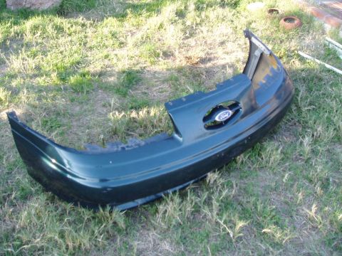 1995 Ford Taurus - A detached green front bumper with a Ford emblem is lying on the grass.