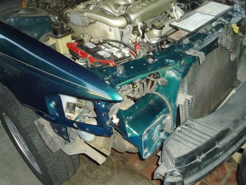 1995 Ford Taurus - The engine compartment of a green 1995 Ford Taurus shows the battery, radiator, and part of the engine, with the front fender removed.