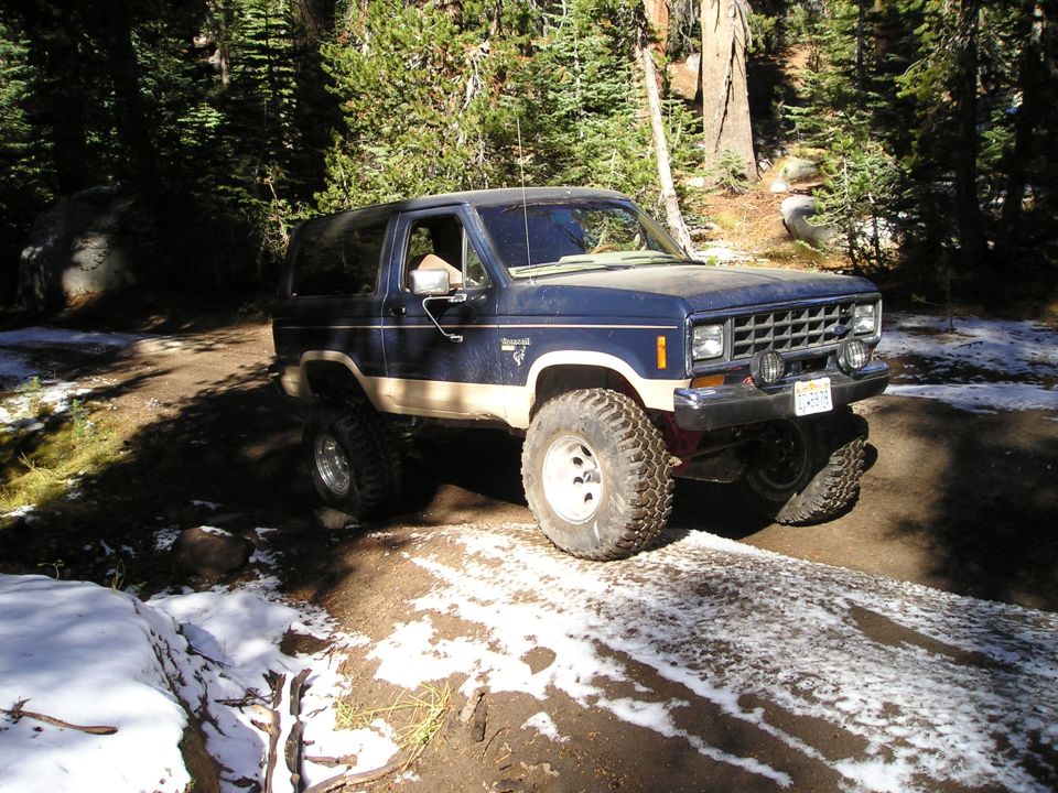 Blue and tan Ford Bronco II on a dirt road with snow patches