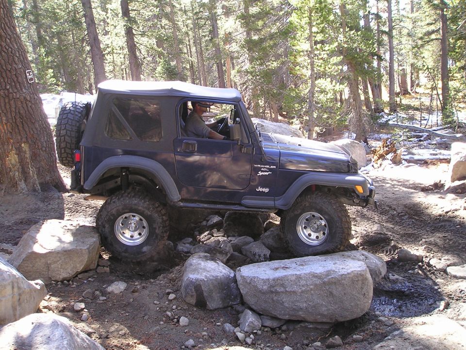 Dark blue Jeep Wrangler TJ navigating rocky terrain