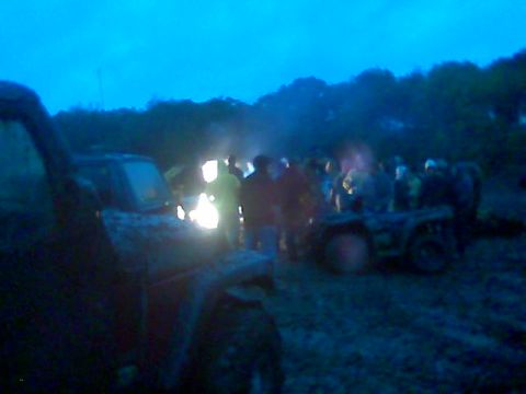 1976 GMC C/K Pickup - A group of people and off-road vehicles are gathered in a muddy field at dusk.