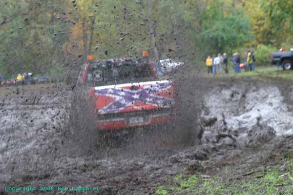 Red pickup truck with confederate flag decal driving through mud