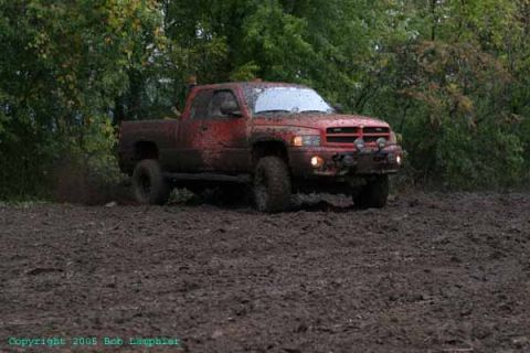 1976 GMC C/K Pickup - A red Dodge Ram pickup truck navigates a muddy terrain, kicking up dirt as it drives.